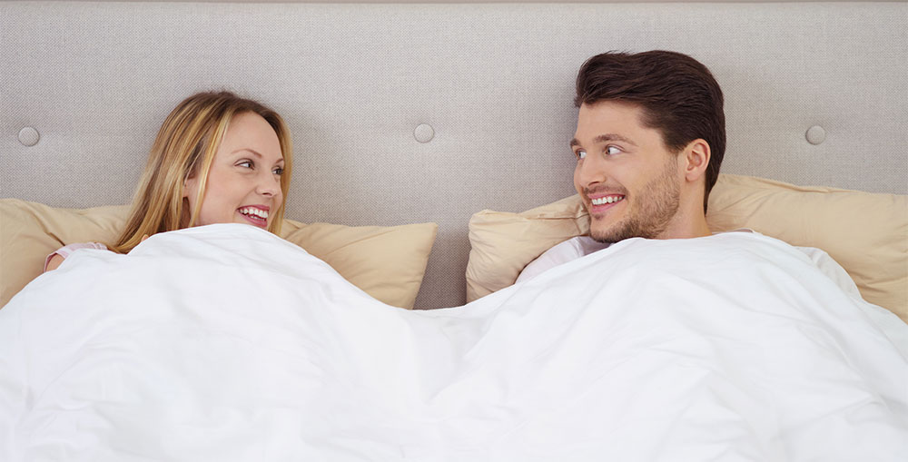 A joyful couple under a THREE Duvets duvet, representing the contentment of a cool, restful night's sleep.
